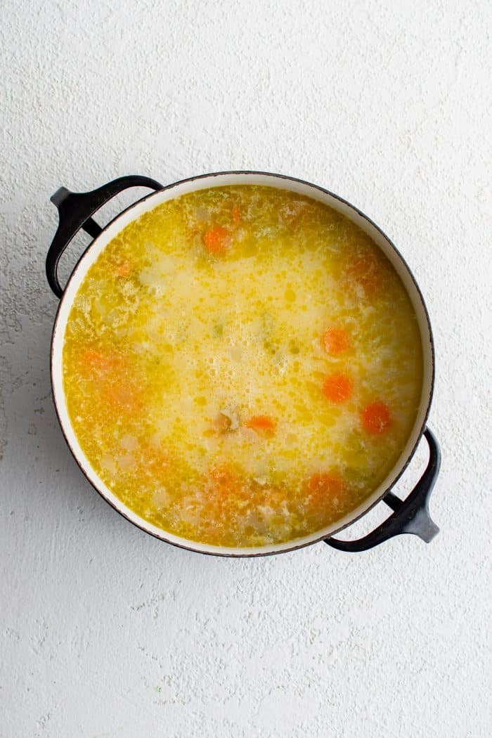 Avgolemono sauce added to a large pot of simmering soup filled with softened veggies and tender white rice.