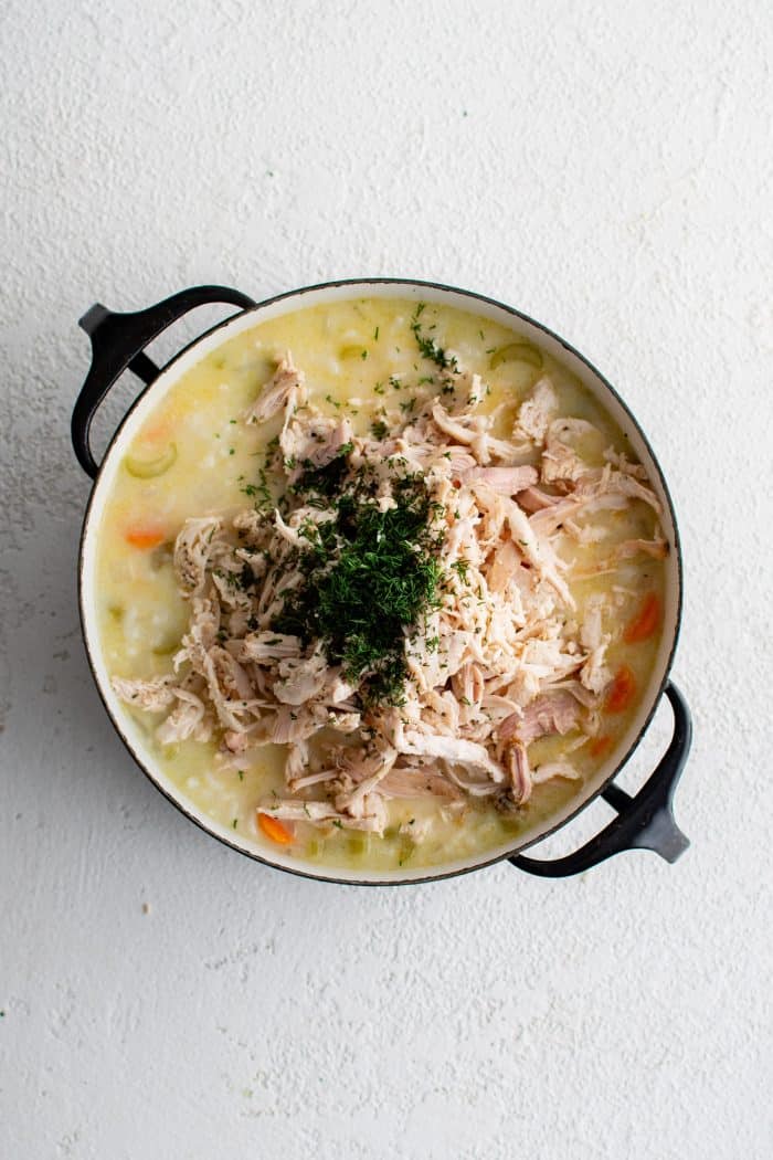 Fresh dill and shredded chicken added to a large pot of avgolemono soup.