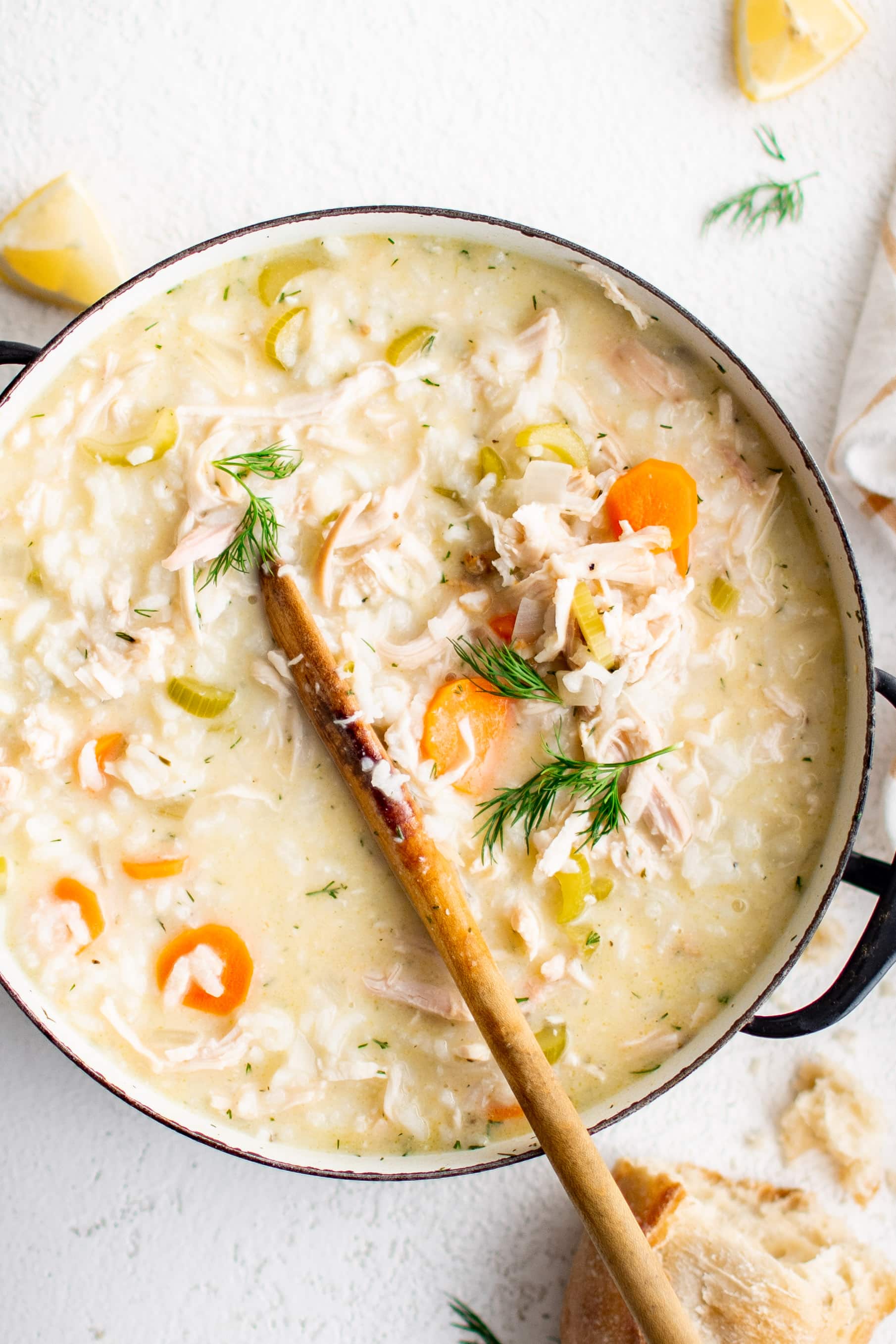 A large ceramic pot filled with simmering Avgolemono Soup made with rice, shredded chicken , carrots, celery, and chicken broth thickened with a mixture of eggs and lemon juice and garnished with fresh dill.
