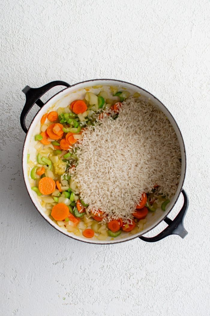 Dry white rice added to a large pot of sauteing onions, carrots, celery, and garlic.