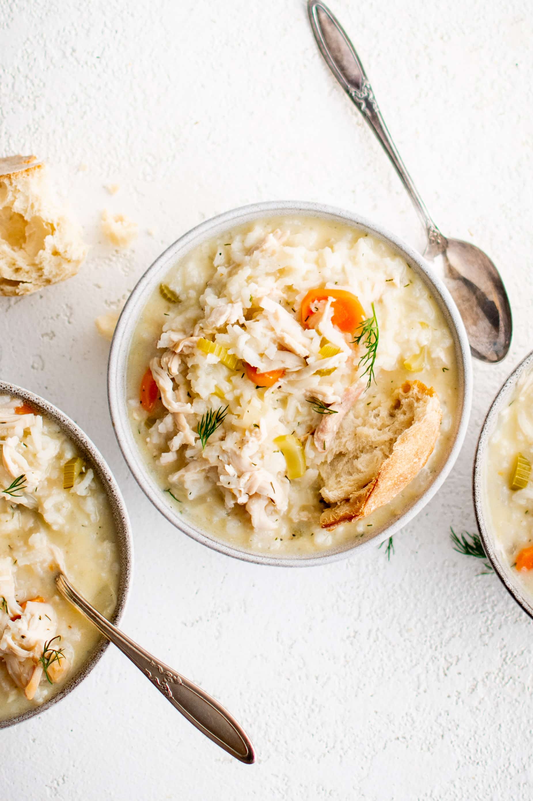 Three white bowls filled with Avgolemono Soup made with rice, shredded chicken , carrots, celery, and chicken broth thickened with a mixture of eggs and lemon juice.