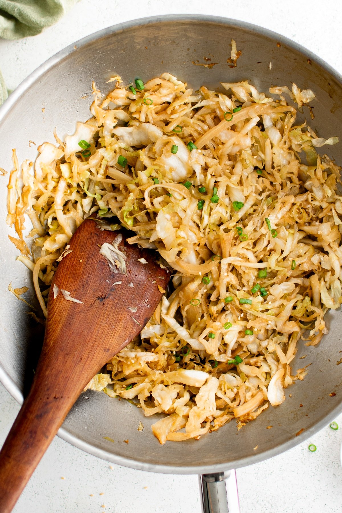 Stir-fried cabbage in a wok with green onions, stirred with a wooden spatula.