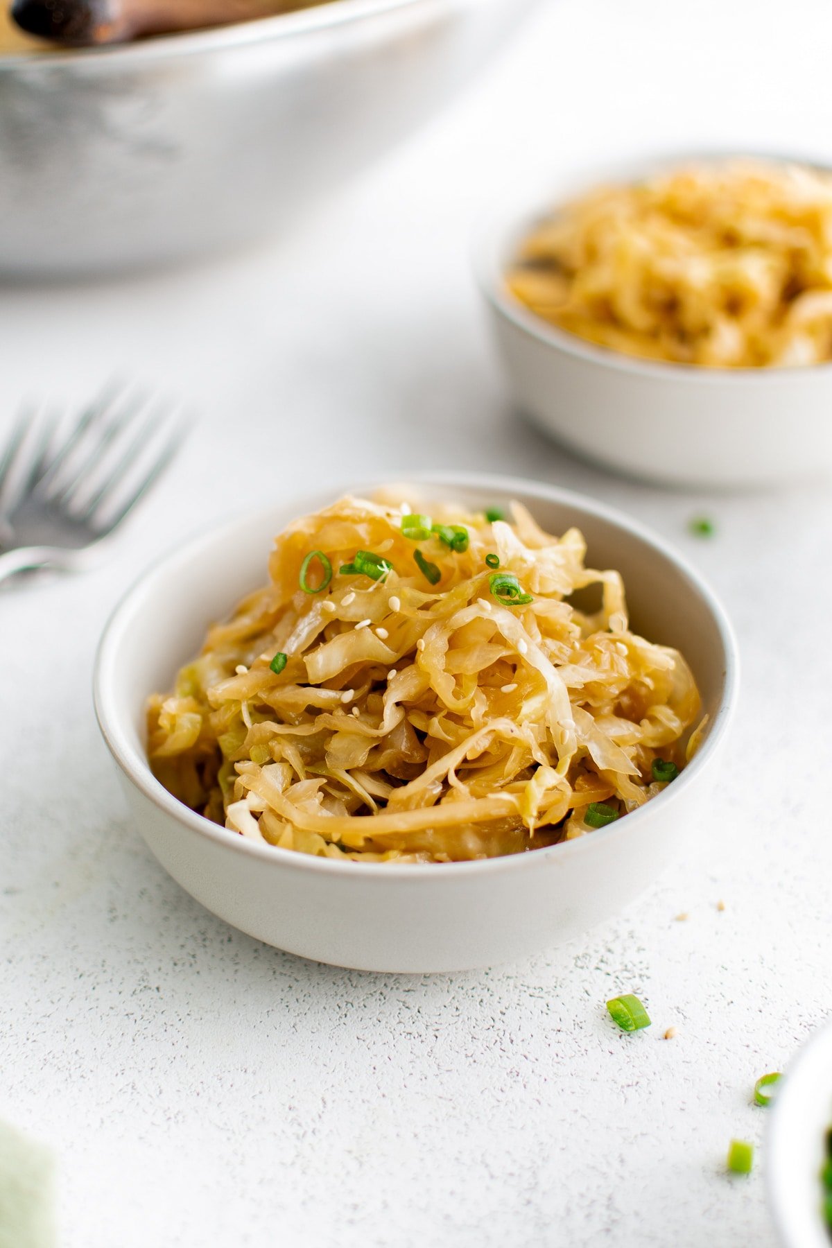 Bowl of stir-fried cabbage topped with sesame seeds and chopped green onions.