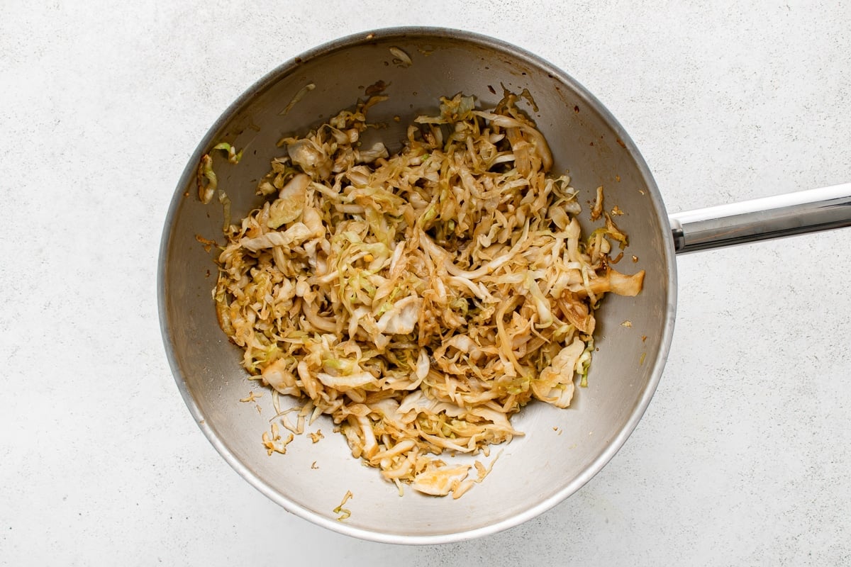 Shredded cabbage cooking in a wok with soy sauce and garlic stir fry sauce.