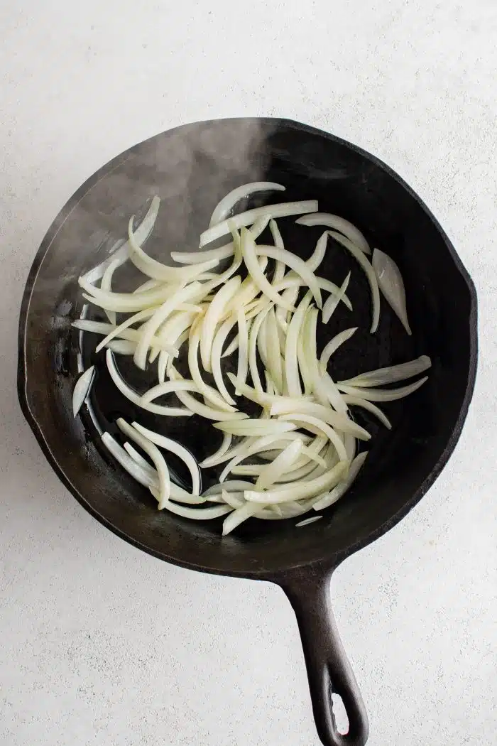 Sliced onions cooking in a large skillet.