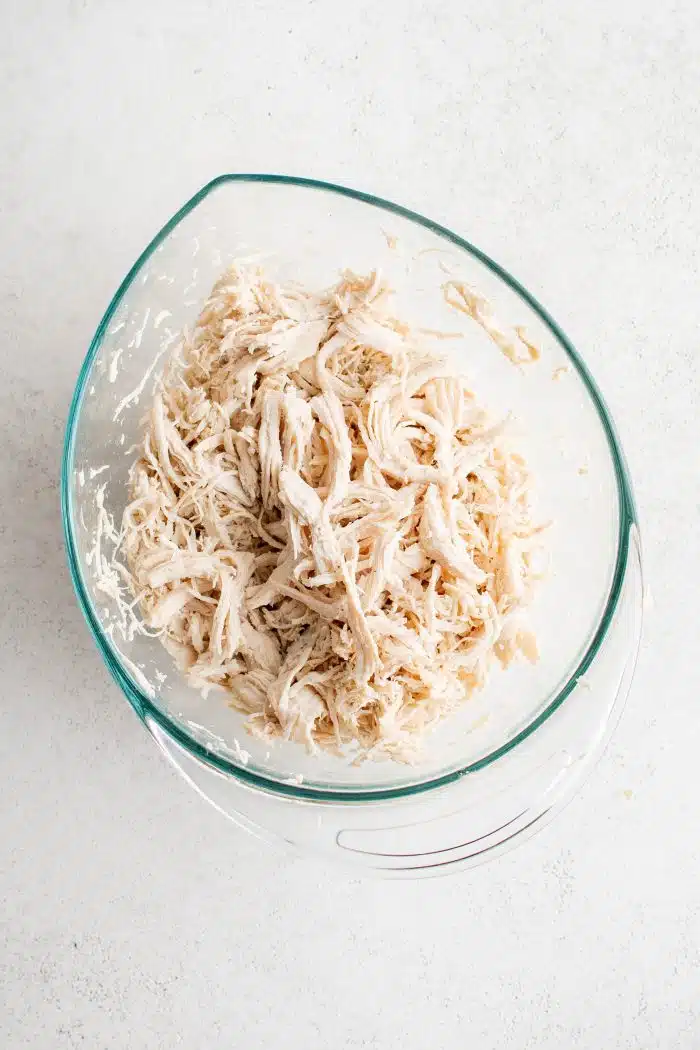 Large glass measuring cup filled with shredded chicken breast meat.