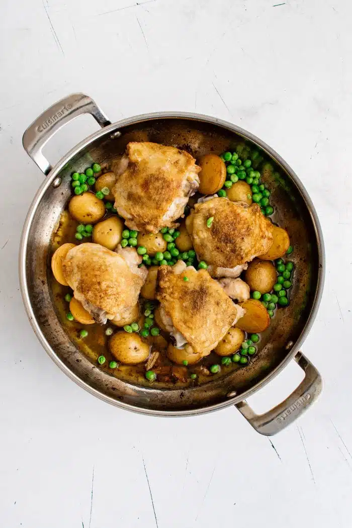 Pan filled with golden brown roasted chicken thighs and potatoes with green peas in a light lemon garlic and white wine sauce.