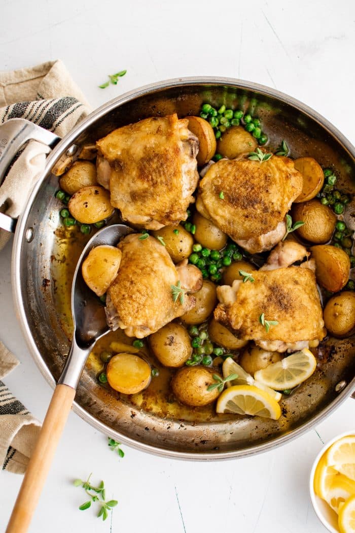Large oven-safe pan filled with cooked chicken vesuvio recipe made with four bone-in skin-on chicken thighs, halved potatoes, garlic, lemon juice, and green peas.