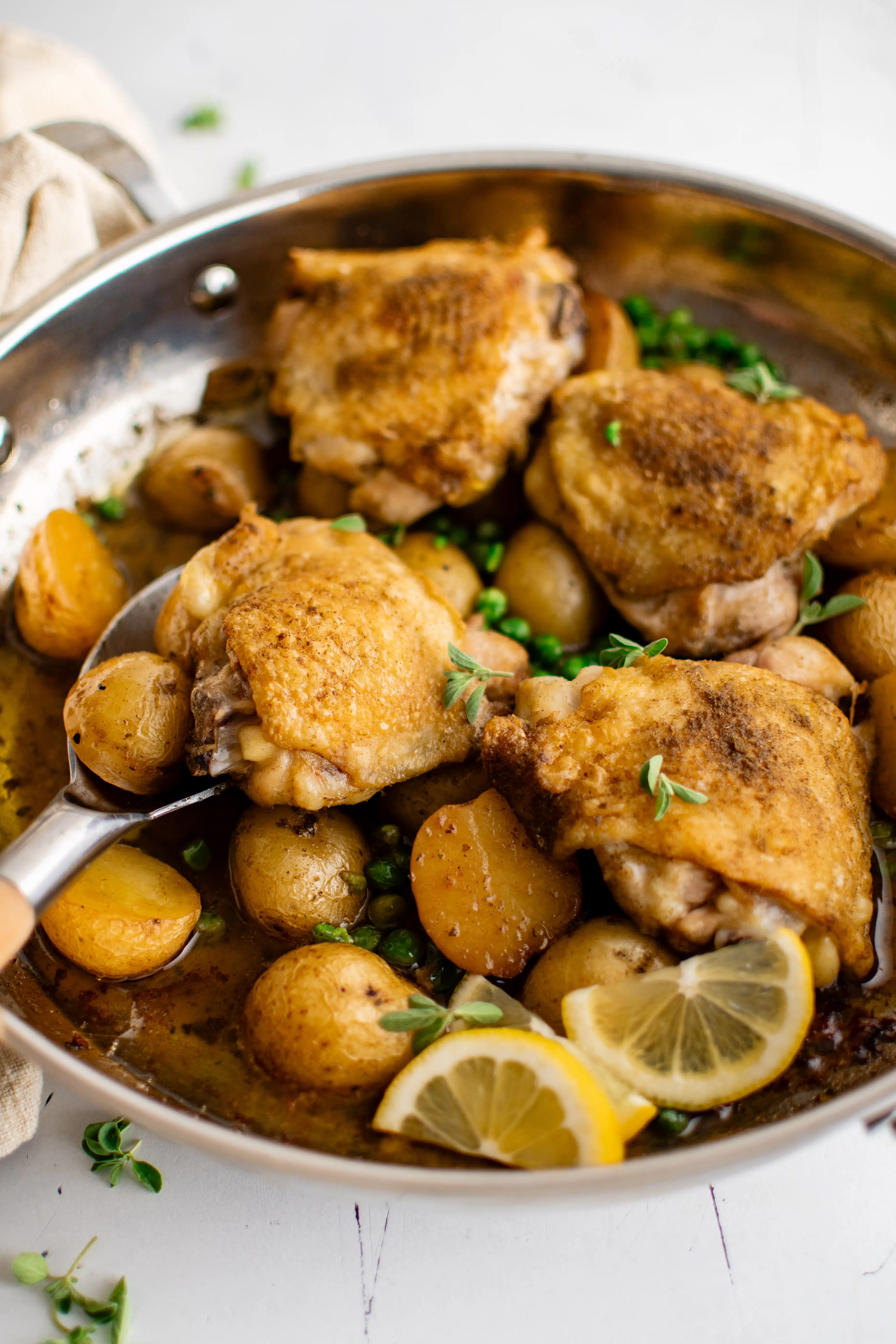 Large oven-safe pan filled with cooked chicken vesuvio recipe made with four bone-in skin-on chicken thighs, halved potatoes, garlic, lemon juice, and green peas.