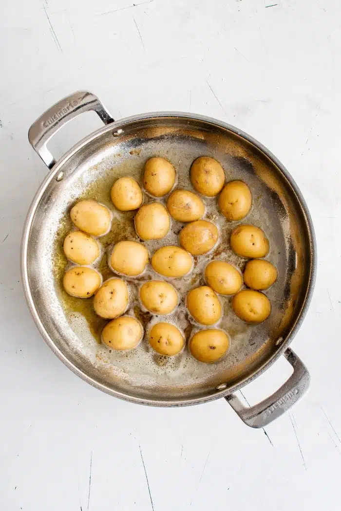 Browning halved Idaho gold potatoes cut side down in a large pan filled with melted butter.