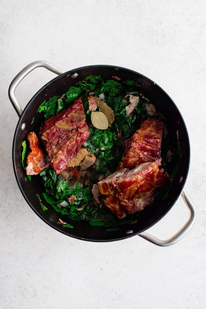 Ham hocks, lemon juice, brown sugar, liquid smoke, bay leaf, salt, black pepper, and paprika, added to a large pot filled with softened diced onion and chopped collard greens and bacon pieces.