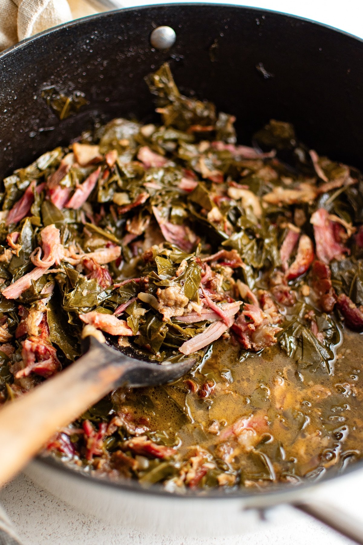 Close-up of Southern-style collard greens simmered with shredded smoked ham and bacon in a cast iron pot
