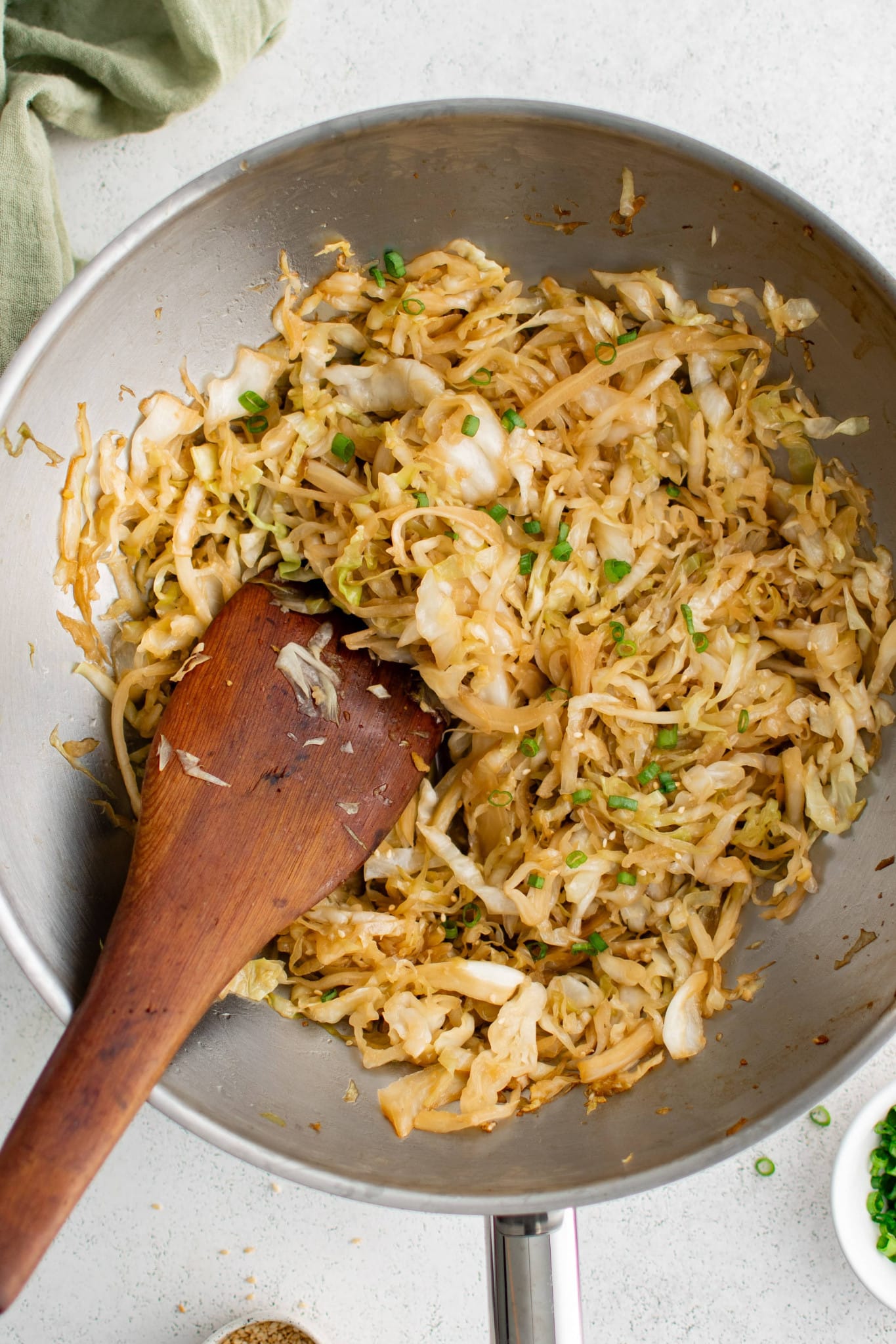 Large stainless steel wok filled with cooked stir-fried cabbage garnished with chopped green onions.
