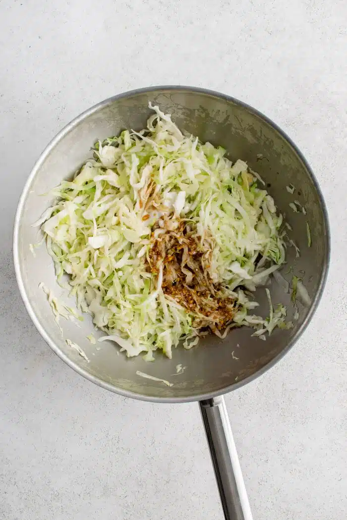 Stir fry sauce poured into the center of a large stainless steel wok filled with shredded green cabbage.