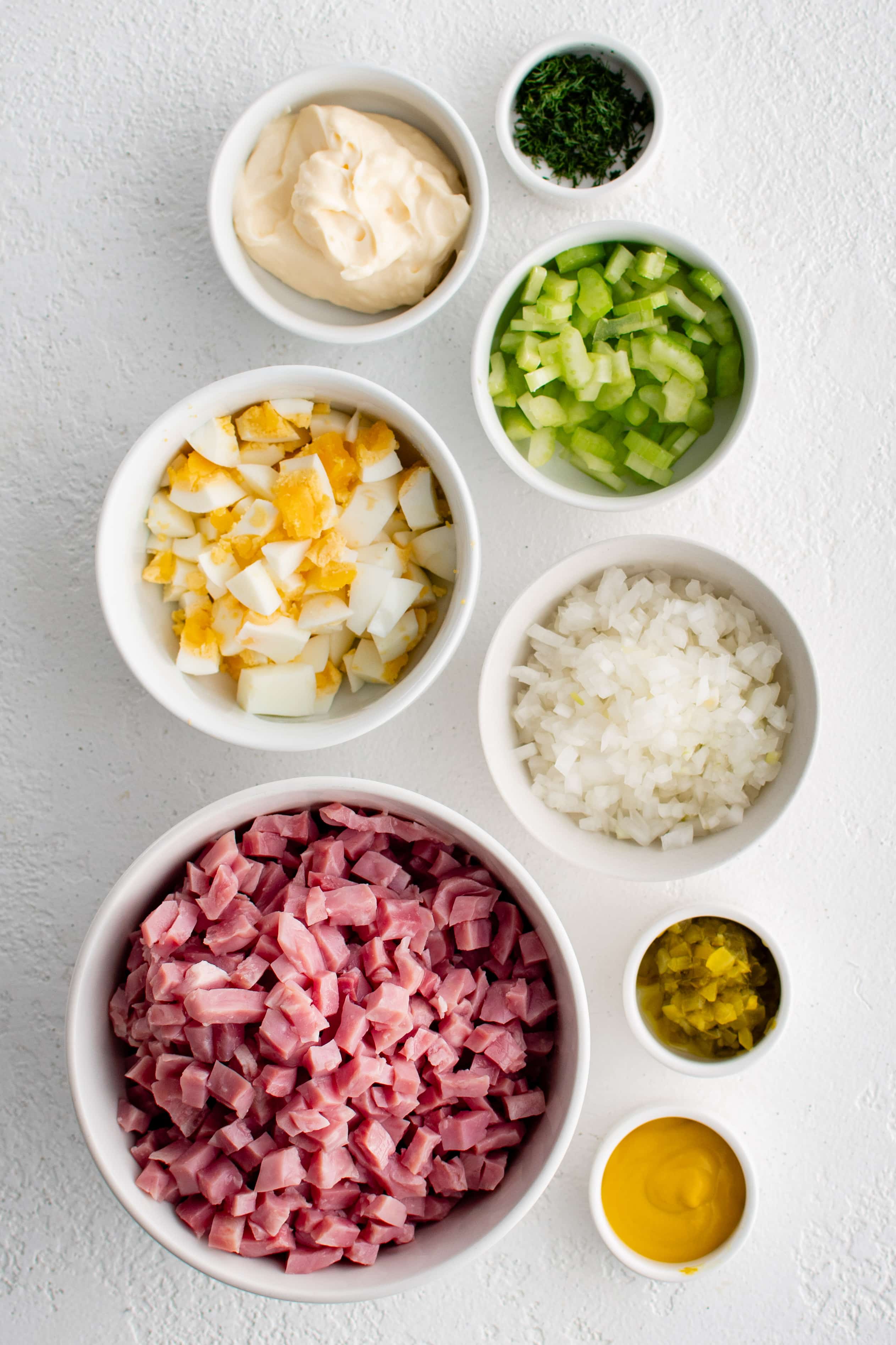Ingredients needed to make ham salad recipe in individual measuring cups and ramekins.