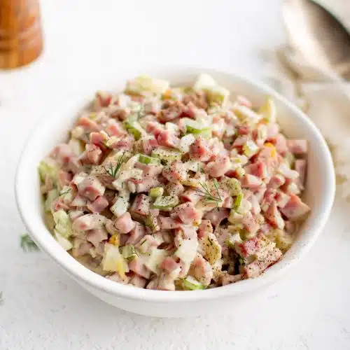 White serving bowl filled with creamy ham salad made with diced pieces of ham, celery, hard-boiled egg, and onion.