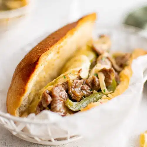 Toasted hoagie roll filled with cheesesteak and green bell pepper in a white deli basket.