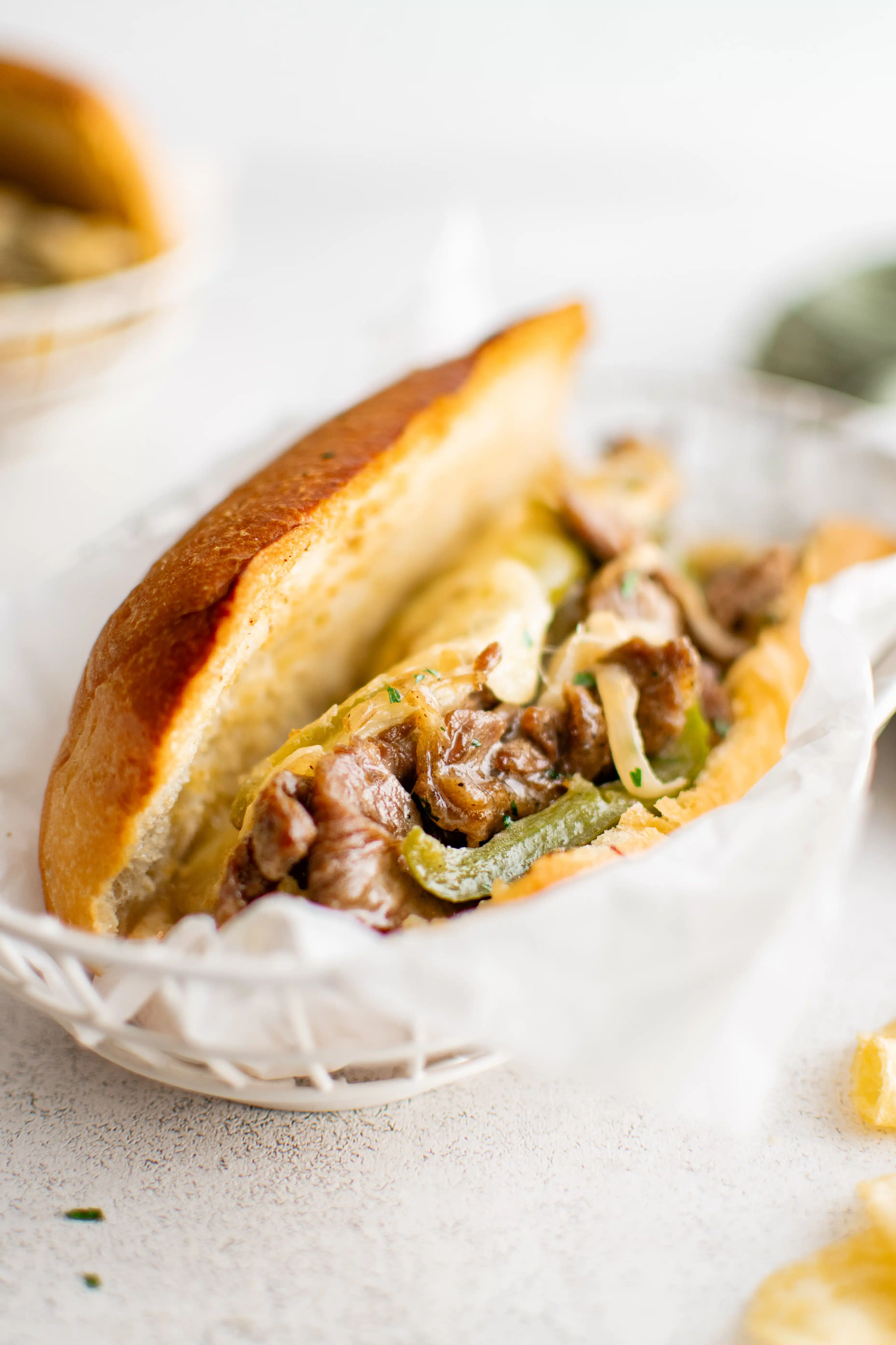 Toasted hoagie roll filled with cheesesteak and green bell pepper in a white deli basket.