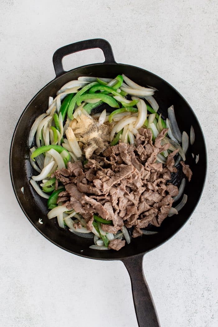 Softened onion and green bell pepper with thinly sliced cooked beef in a large cast iron skillet.