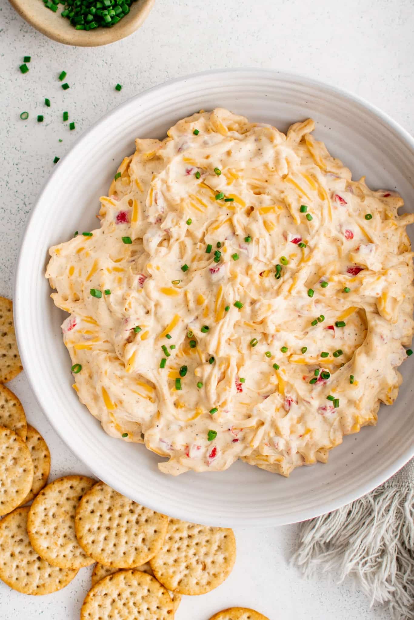 Large shallow mixing bowl filled with pimento cheese dip garnished with freshly chopped chives and served with crackers on the side.