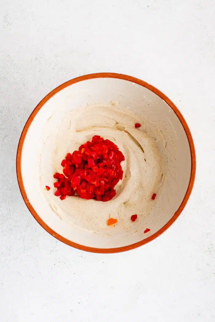 White bowl with smooth and creamy cream cheese and mayo combination seasoned with paprika, salt, and black pepper, topped with diced pimentos.