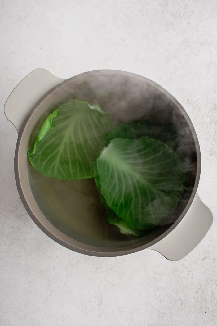 Outer cabbage leaves boiling in a large pot of boiling water.