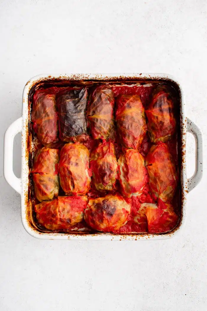 White baking dish filled with cabbage rolls stuffed with ground beef, pork, and rice and covered in tomato sauce.