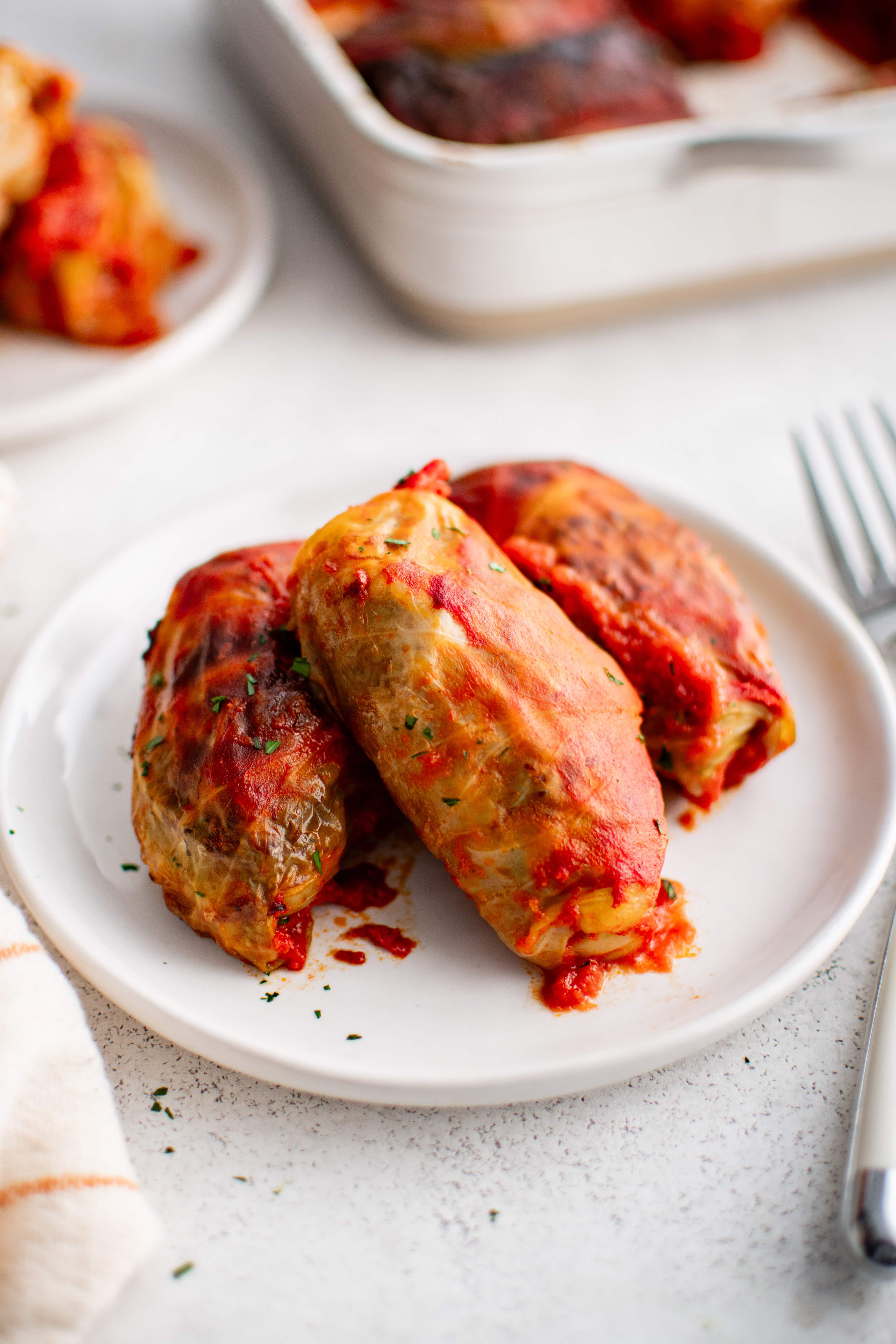 Three pork, beef, and rice stuffed cabbage rolls on a white dinner plate covered in tomato sauce.