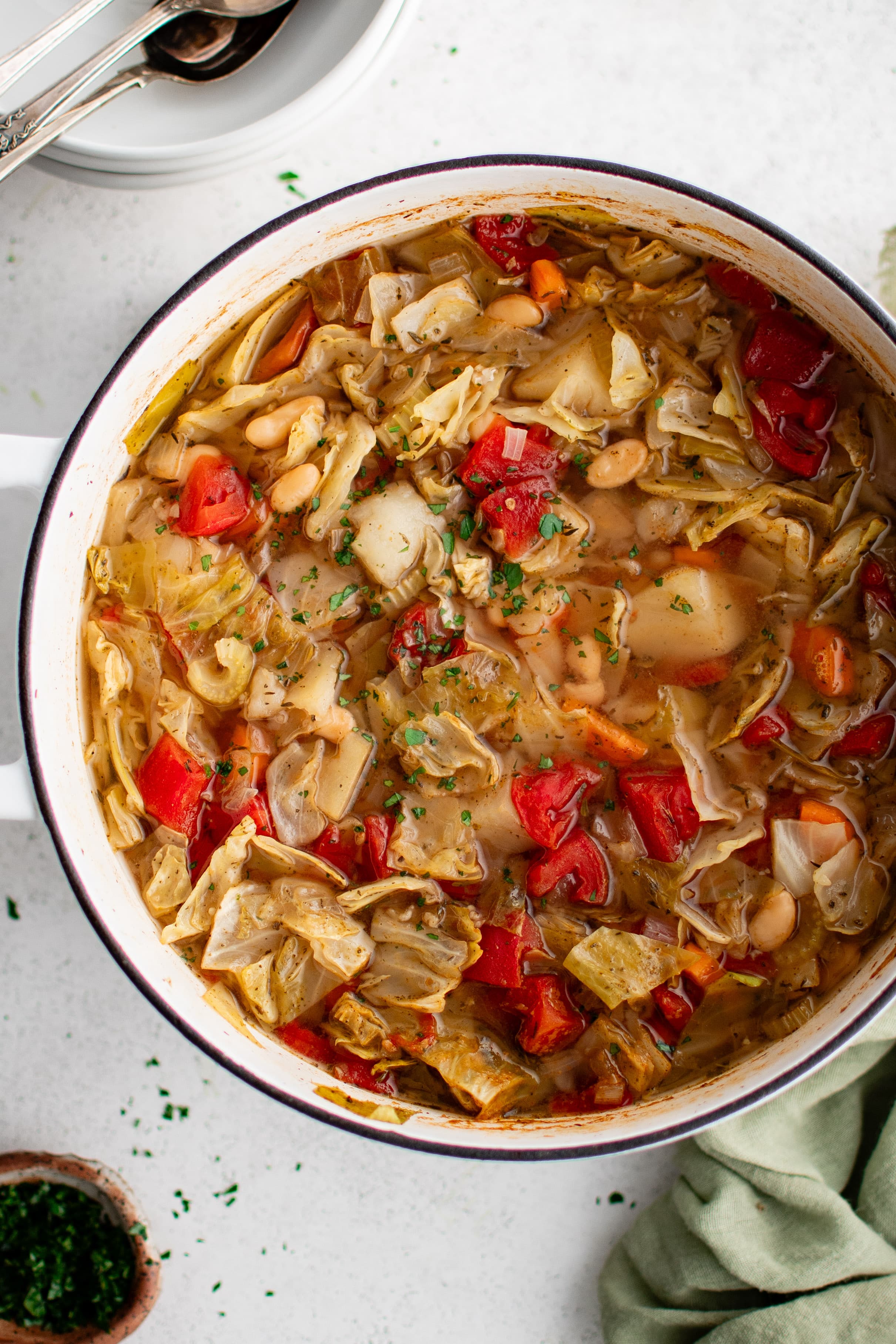 Large Dutch oven filled with simmering cabbage soup filled with with vegetable cabbage soup that's filled with potatoes, tender cabbage, tomatoes, white beans, carrots, onion, and celery, in a herbed vegetarian broth and sprinkled with minced parsley.