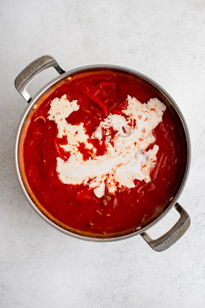 Heavy cream added to a large stainless steel pot filled with tomato sauce with sliced bell peppers, onion, and hot cherry peppers.