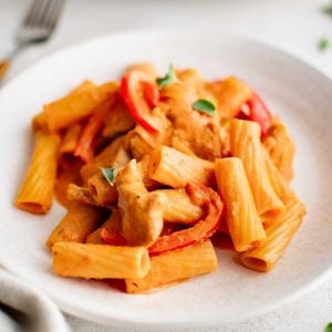 White plate filled with chicken riggies pasta with sliced red bell pepper and garnished with fresh parsley.