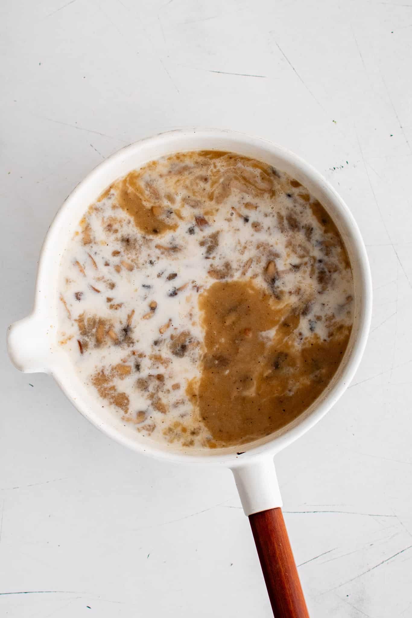 Milk added to a white pot filled with diced caramelized onions in beef broth.