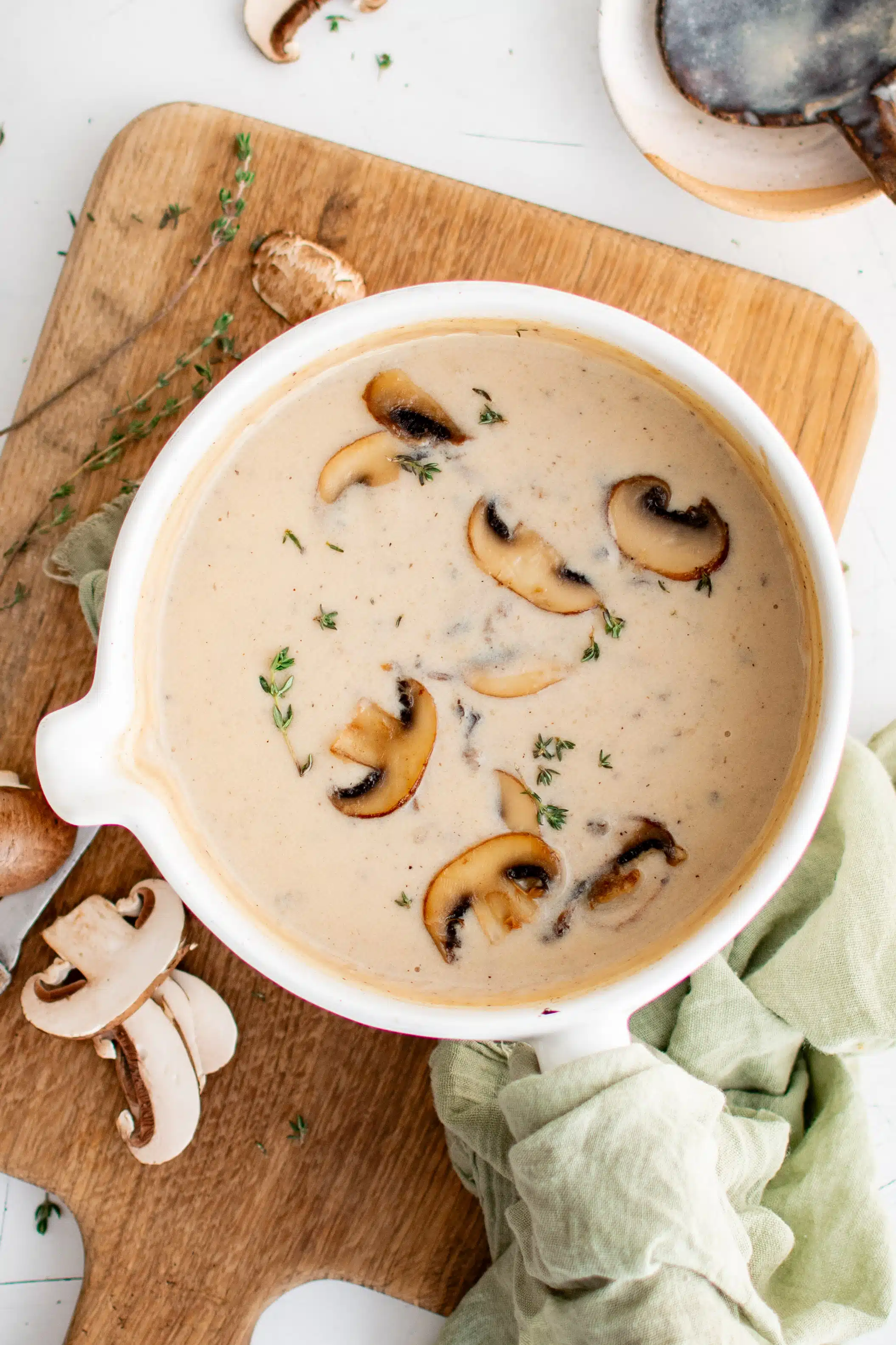 White Dutch oven filled with cream of mushroom soup and topped with caramelized sliced mushrooms and fresh thyme.