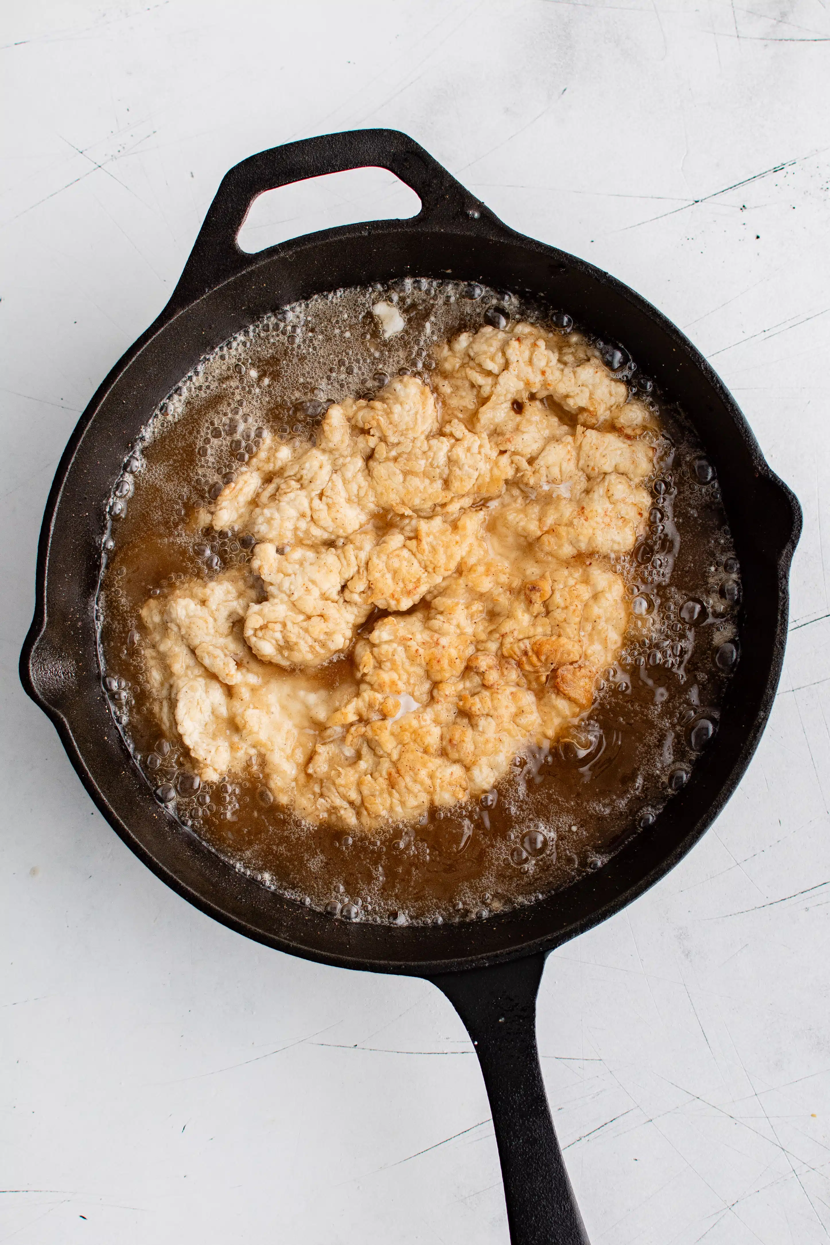 Breaded chicken breast pan-frying in a large skillet filled with vegetable oil.