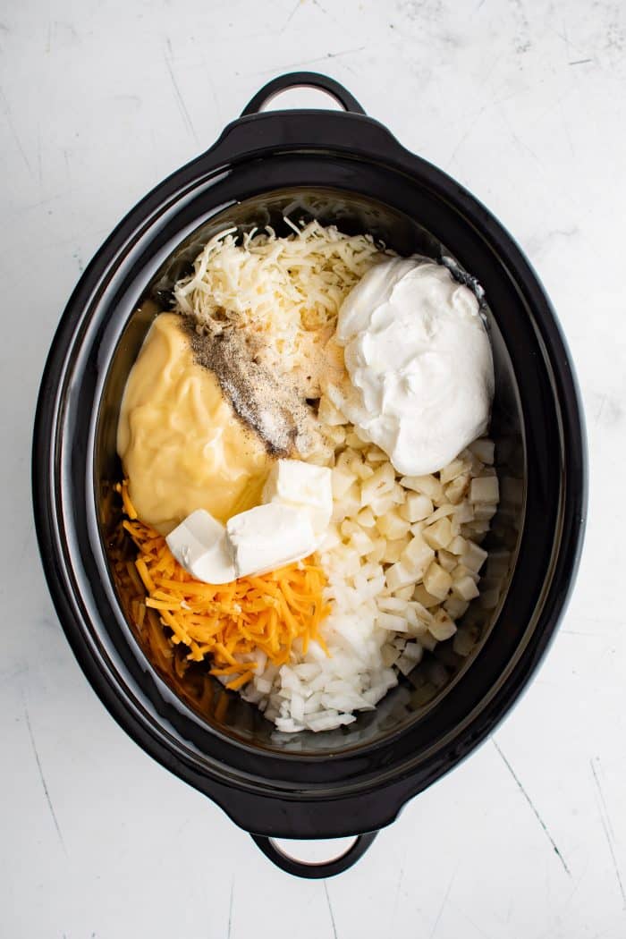 Large slow cooker filled with the ingredients required to make Crockpot cheesy potatoes.