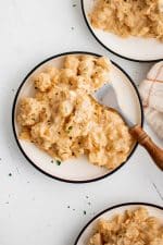 Three plates with a black rim filled with Crockpot cheesy potatoes and garnished with minced parsley.