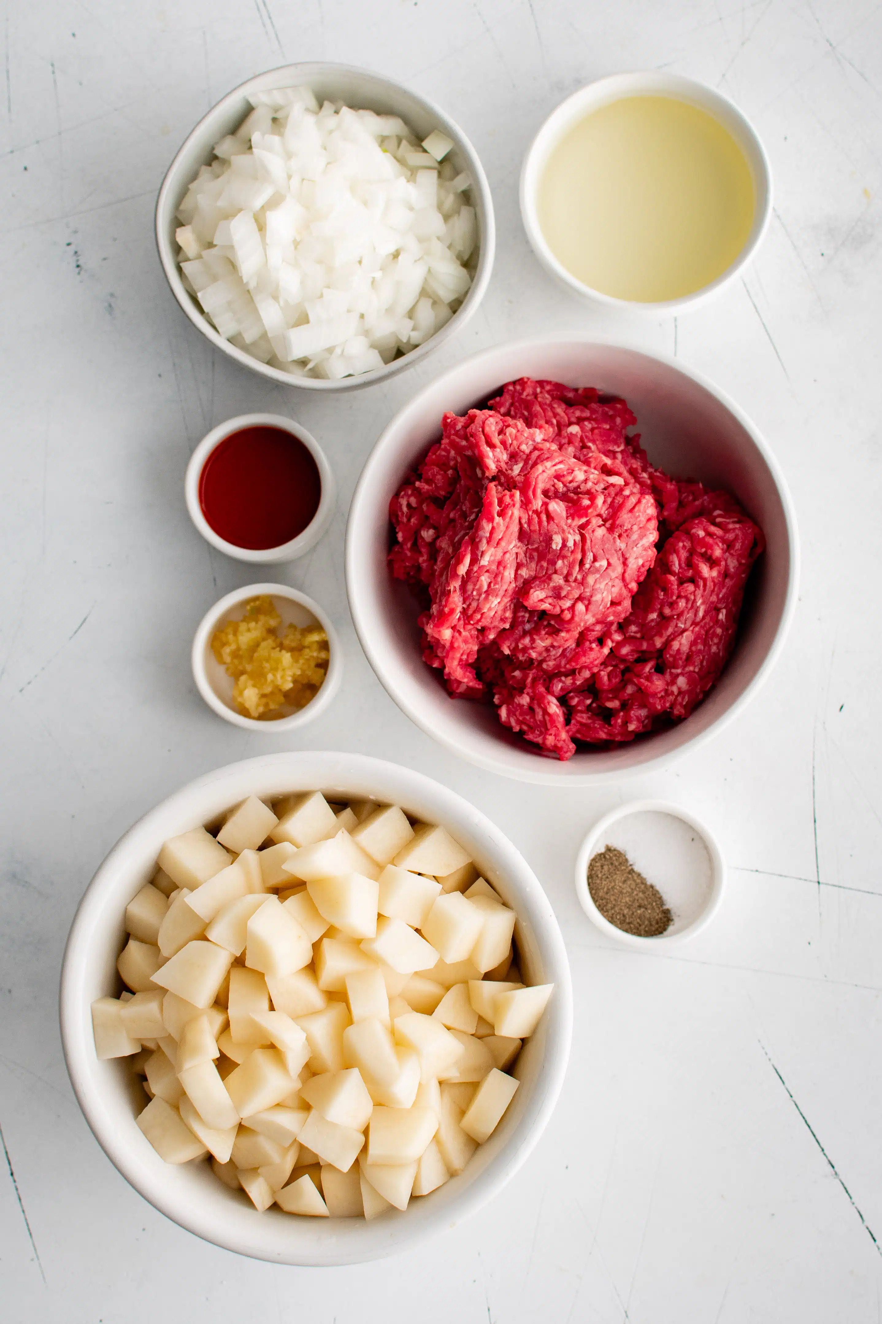 Ingredients needed to make ground beef and potatoes in individual measuring cups and ramekins.