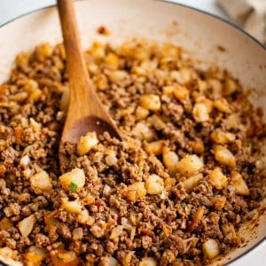 Large skillet filled with cooked ground beef with onion and diced potatoes.