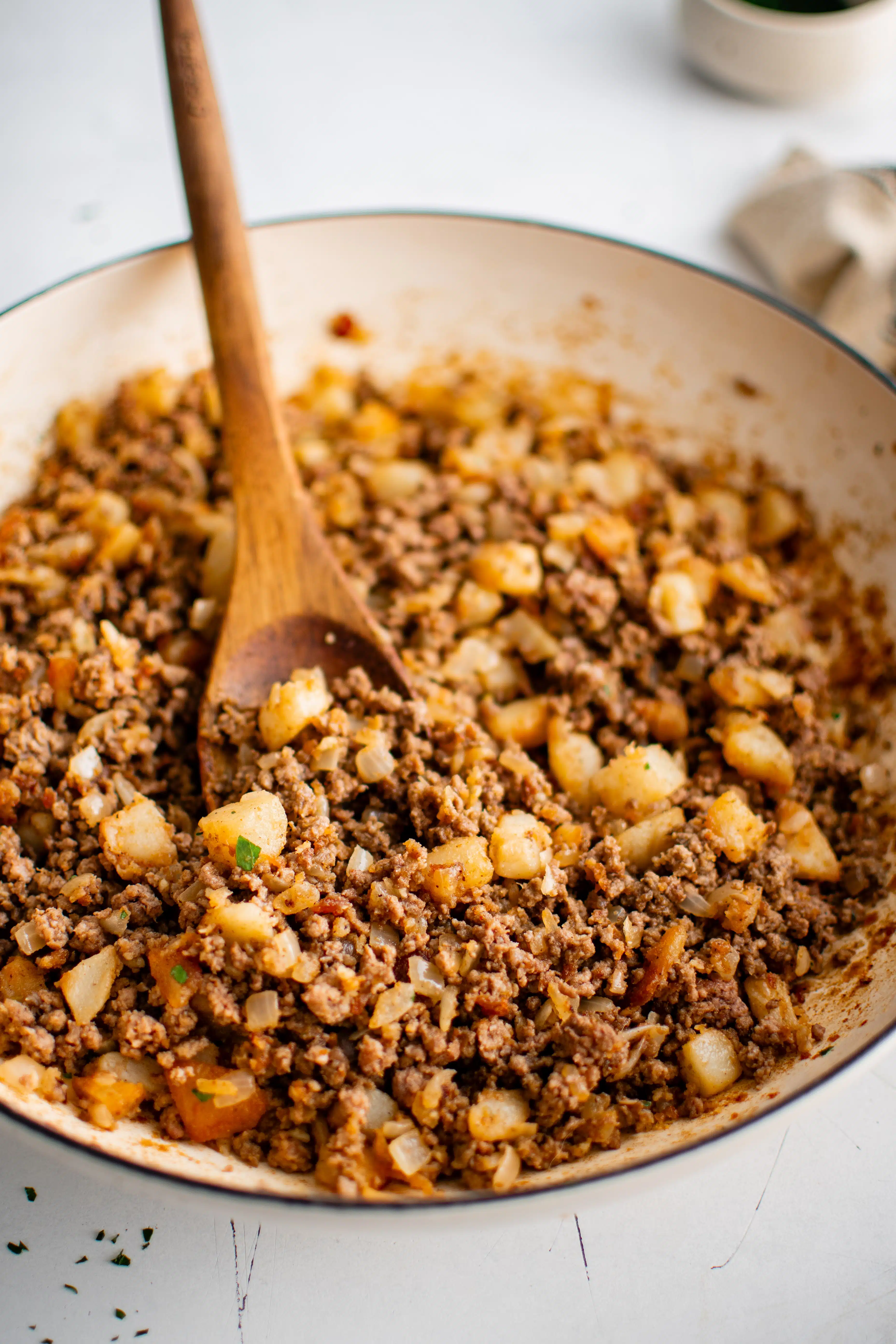 Large skillet filled with cooked ground beef with onion and diced potatoes.