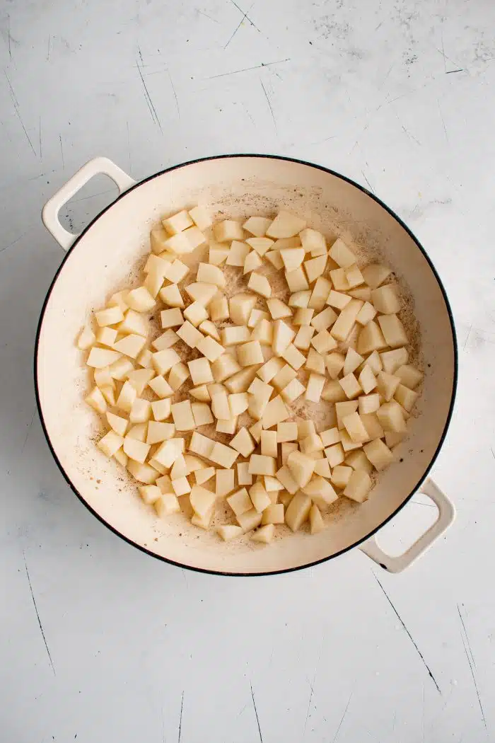 Small cubed potatoes cooking in a large ceramic skillet.