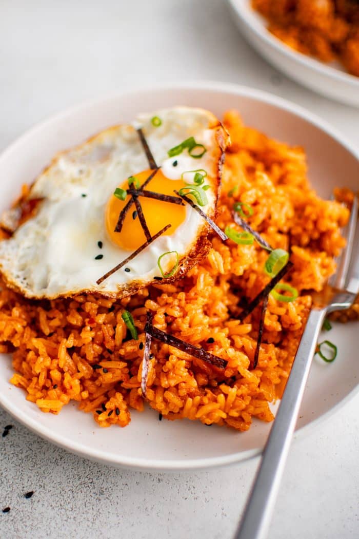 With plate with a serving of kimchi fried rice and topped with a single fried egg and garnished with sliced green onions, sliced seaweed, and black sesame seeds.