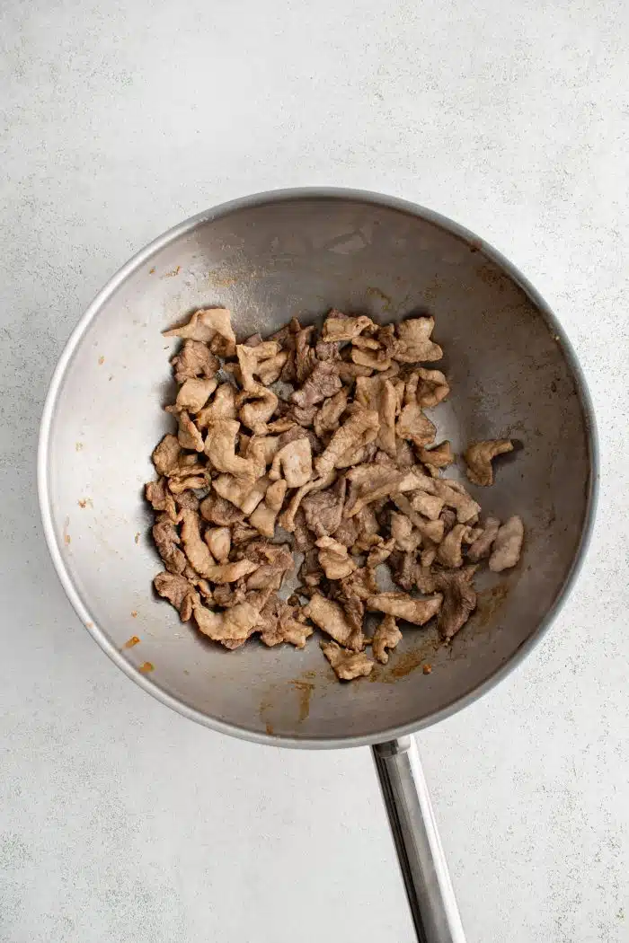 Large wok filled with cooked slices of stir fried pork tenderloin.