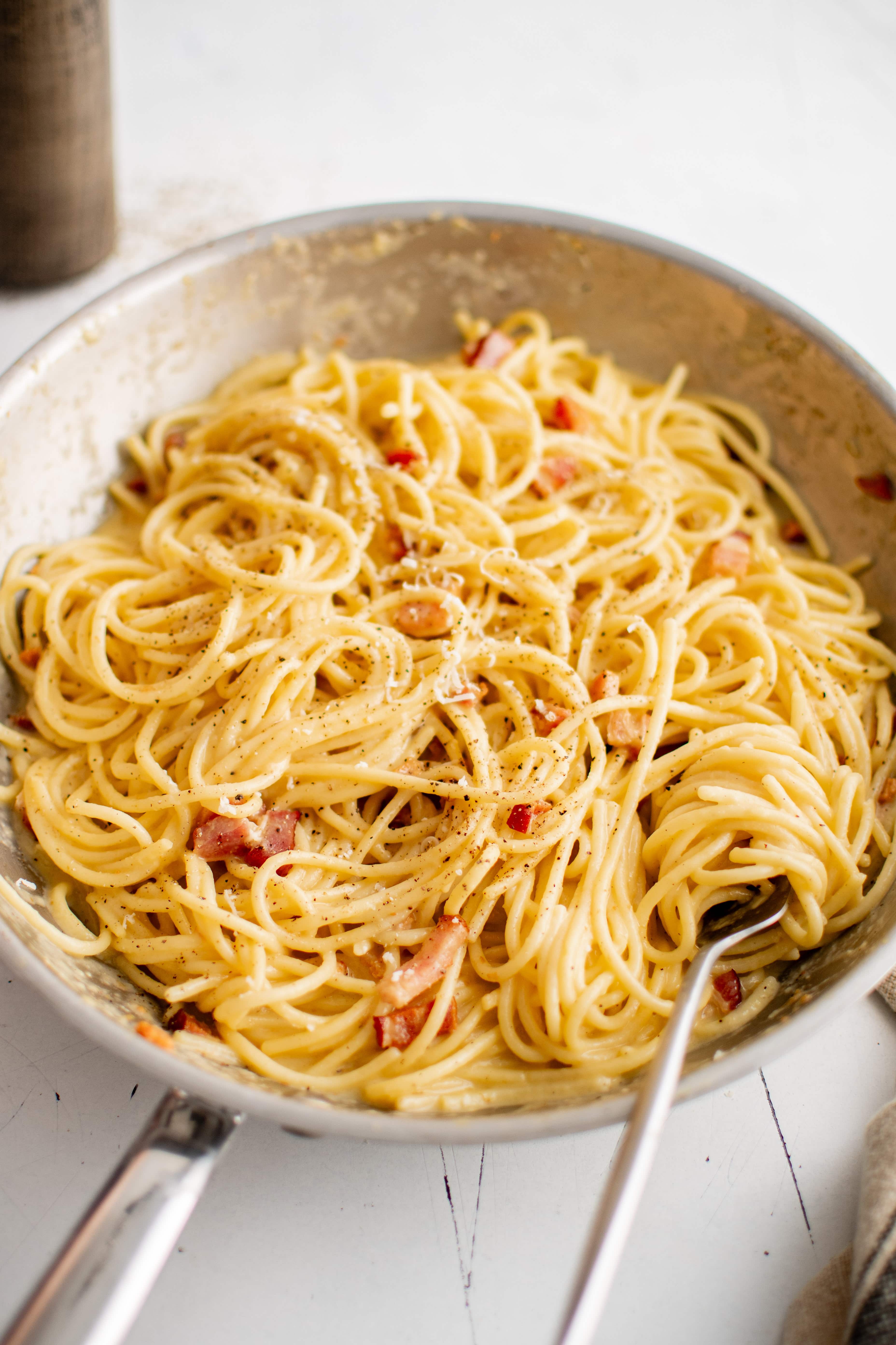 Large skillet filled with luscious spaghetti carbonara with bacon.