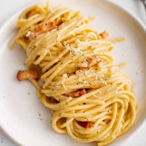 White plate plated with a serving of freshly cooked spaghetti carbonara.