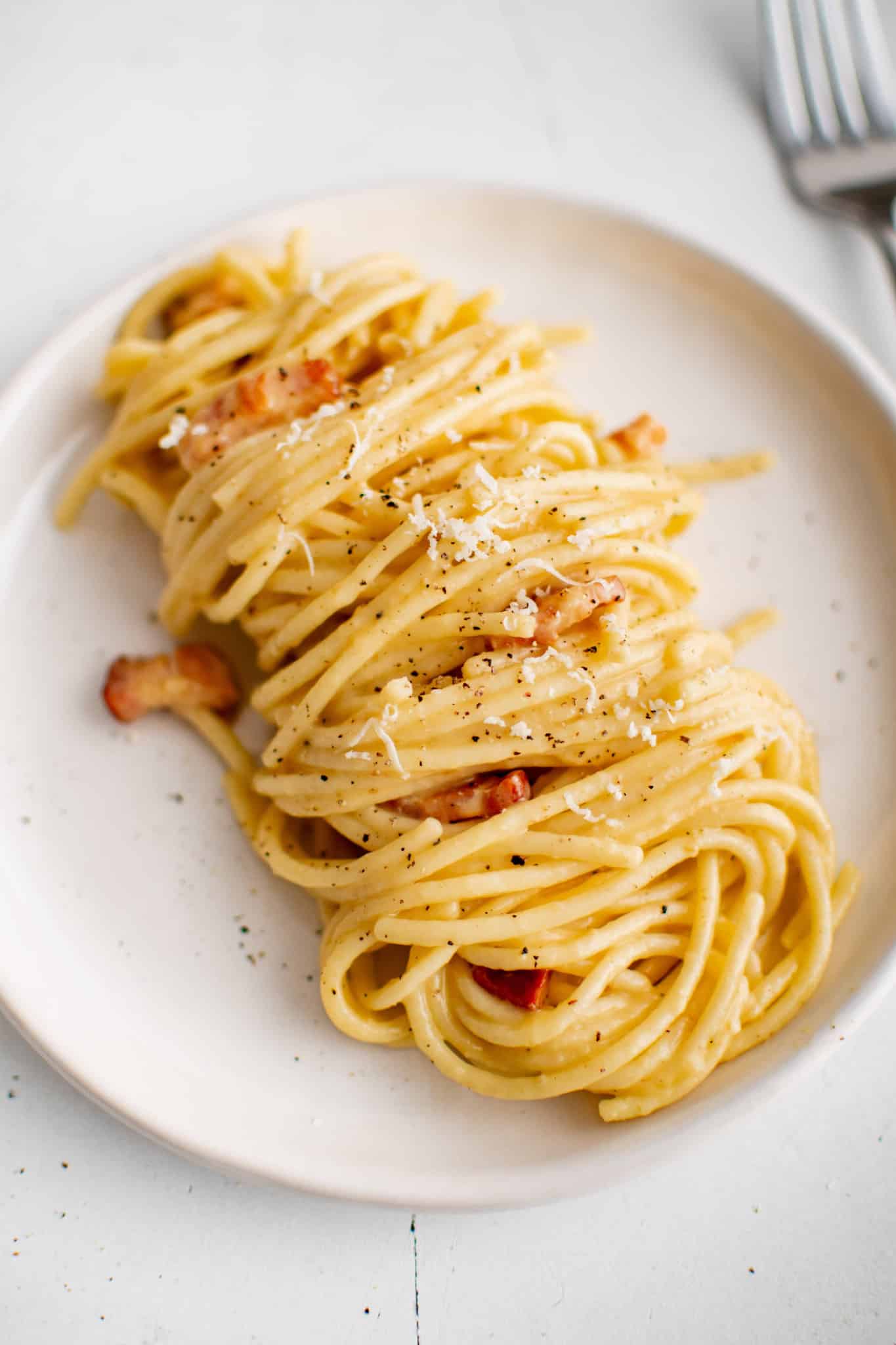 White plate plated with a serving of freshly cooked spaghetti carbonara.