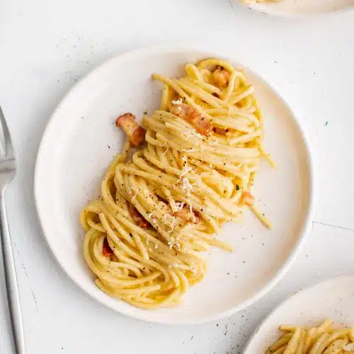 White plate plated with a serving of freshly cooked spaghetti carbonara.