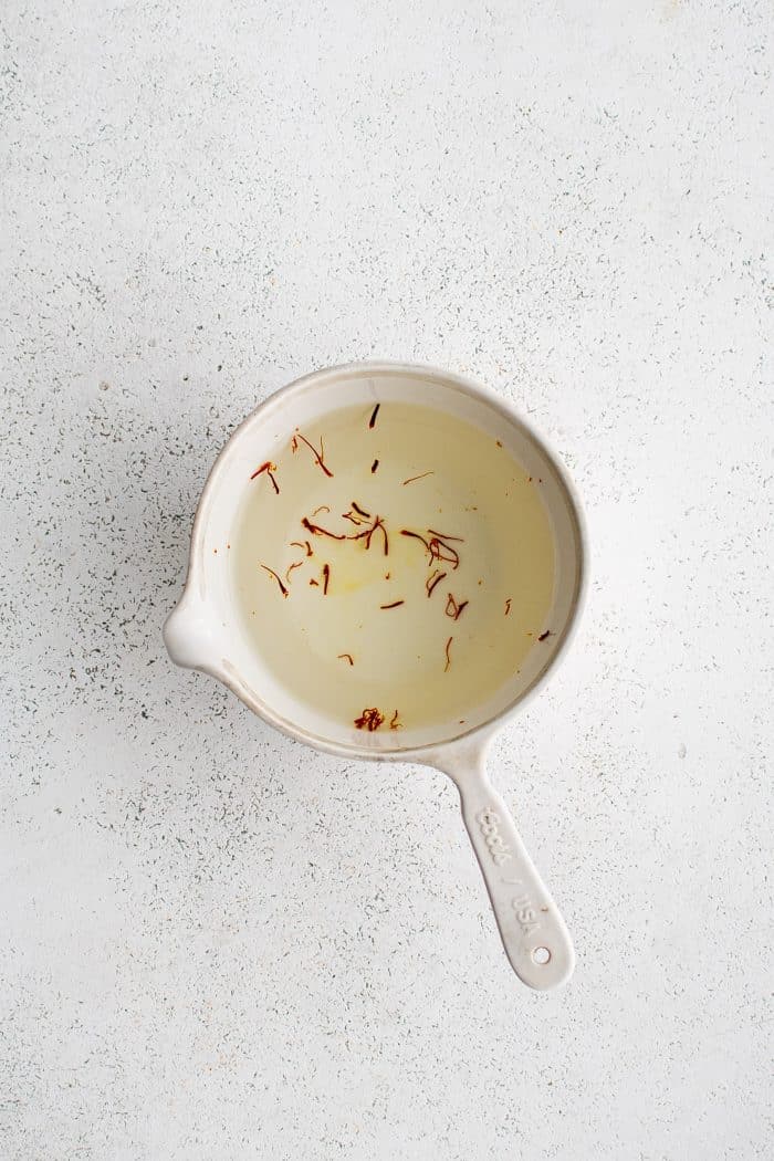 White measuring cup filled with boiling water and saffron threads.