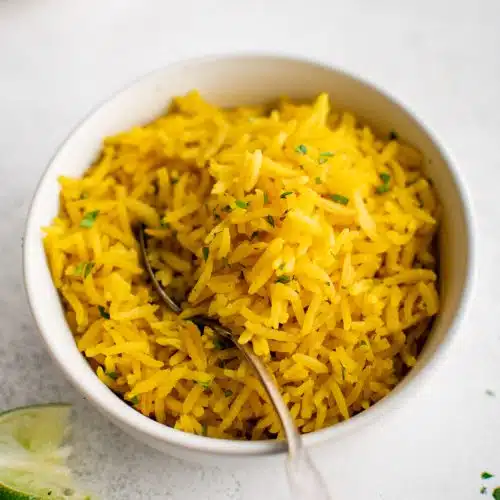 Large shallow bowl filled with cooked yellow rice and garnished with lime wedges.