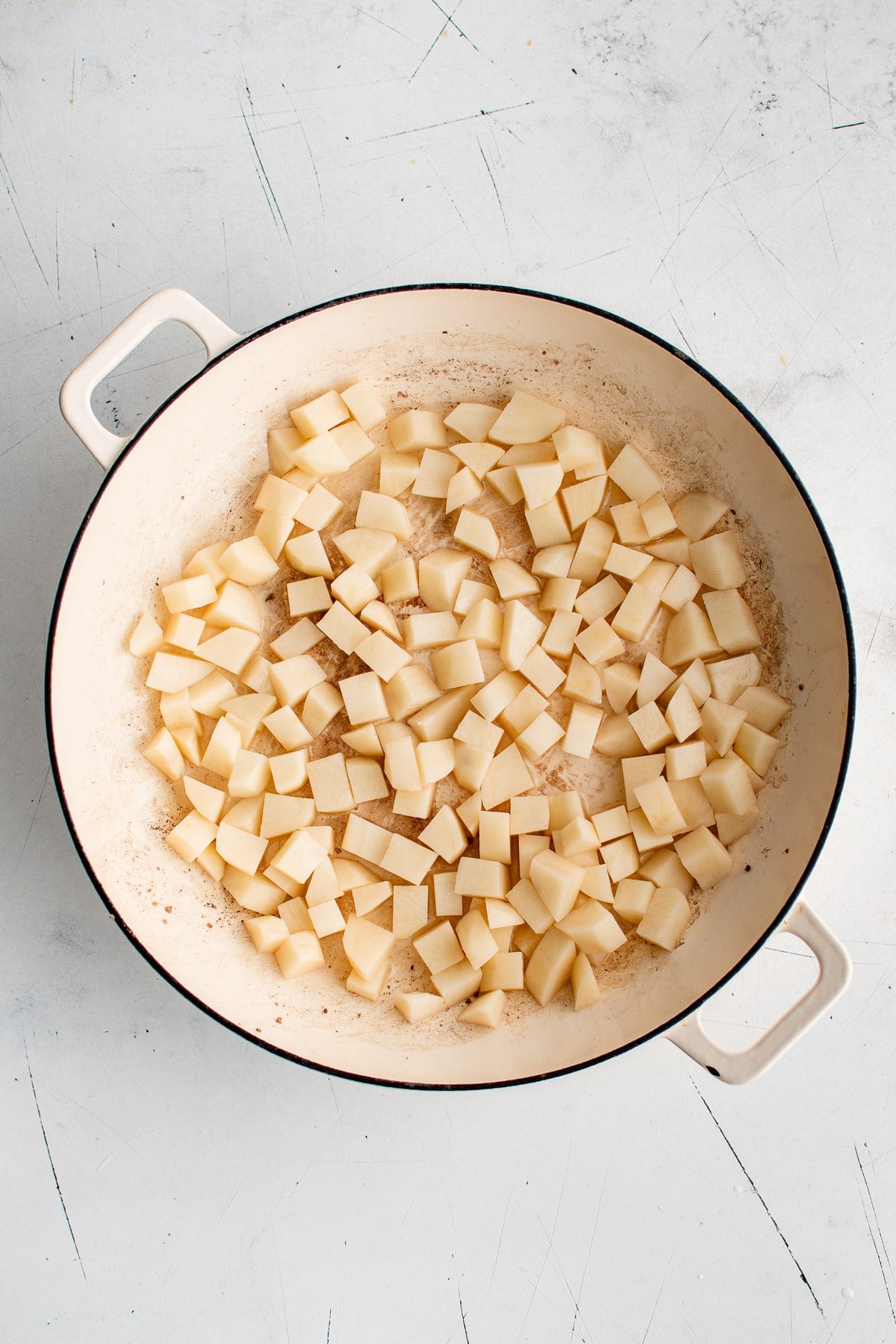 Overhead view of peeled and diced Yukon Gold potatoes spread across the bottom of a cream-colored enameled cast iron braiser.