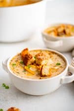 Two white soup bowl filled with cheeseburger soup garnished with hamburger bun croutons, shredded cheddar cheese, and chopped green onions.